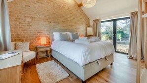 Quarto com cama grande, mesa de cabeceira, abajur, espelho e vista para o exterior.