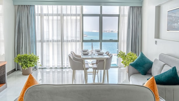 A modern living room with a dining area, large windows with curtains, a sofa, and two potted plants. - Marukab Plaza (Malé)