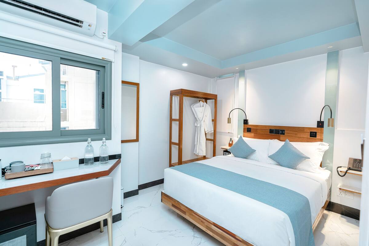 Une chambre d’hôtel moderne, équipée d’un lit, d’un bureau, d’une chaise et d’une fenêtre.