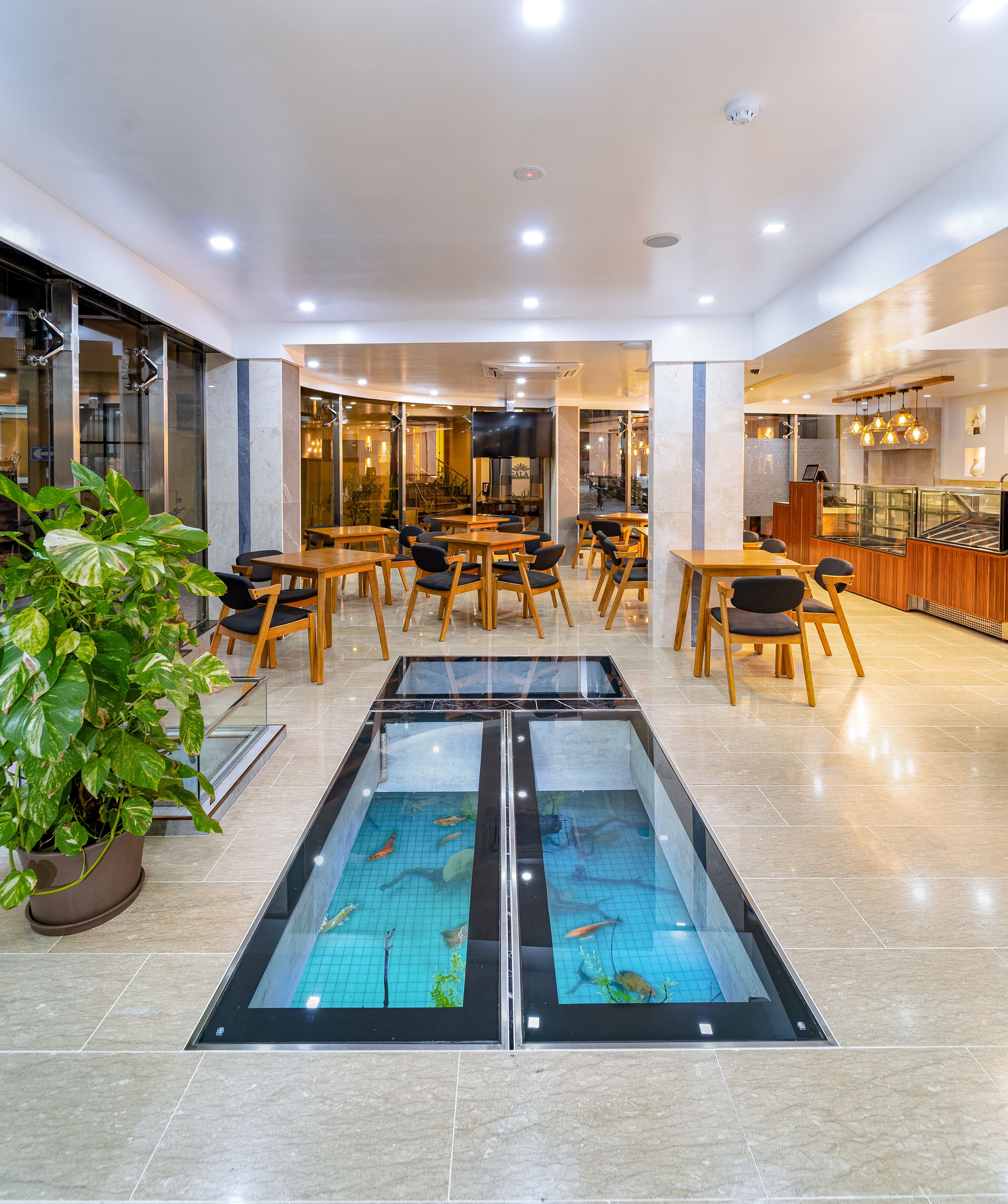 A modern hotel lobby with a central aquarium, wooden tables, and chairs.