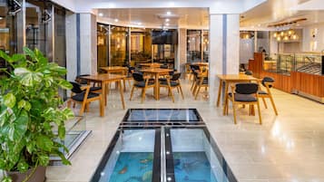 A modern hotel lobby with a central aquarium, wooden tables, and chairs.