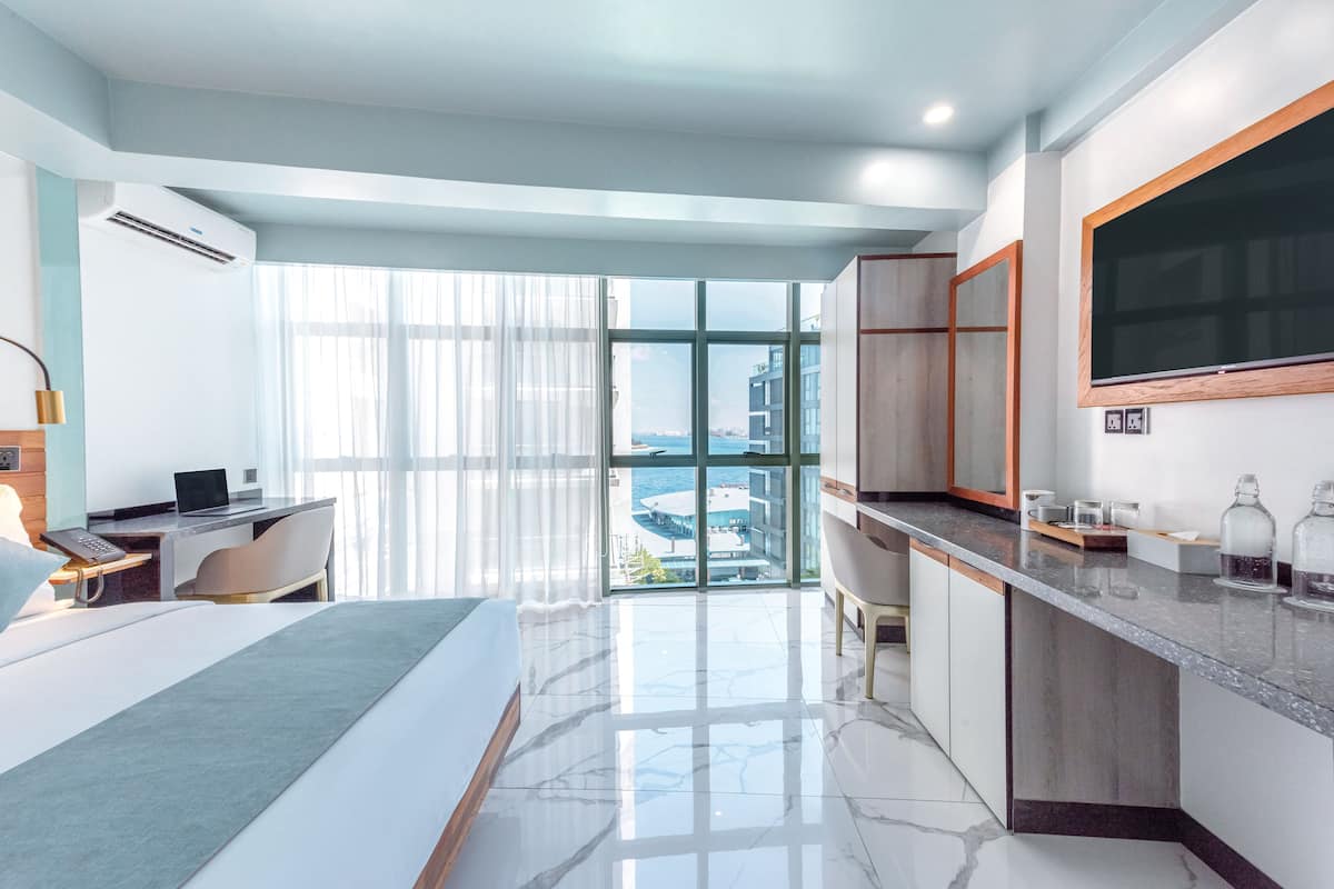 Une chambre d’hôtel moderne dotée d’un grand lit, d’un bureau et offrant une vue sur la ville grâce à de grandes fenêtres du sol au plafond.