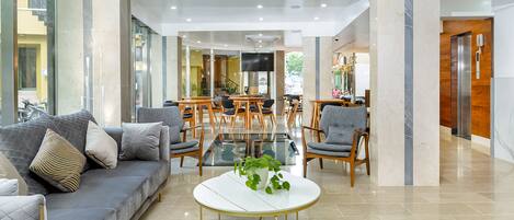 A modern hotel lobby with a grey sofa, round tables, and a staircase leading to an upper floor.