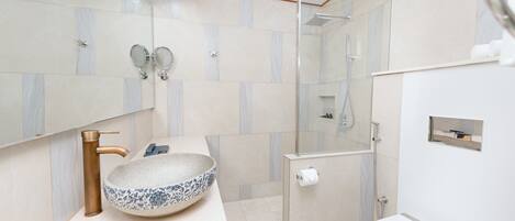 A modern bathroom with a large vessel sink, a handheld showerhead, and a toilet.