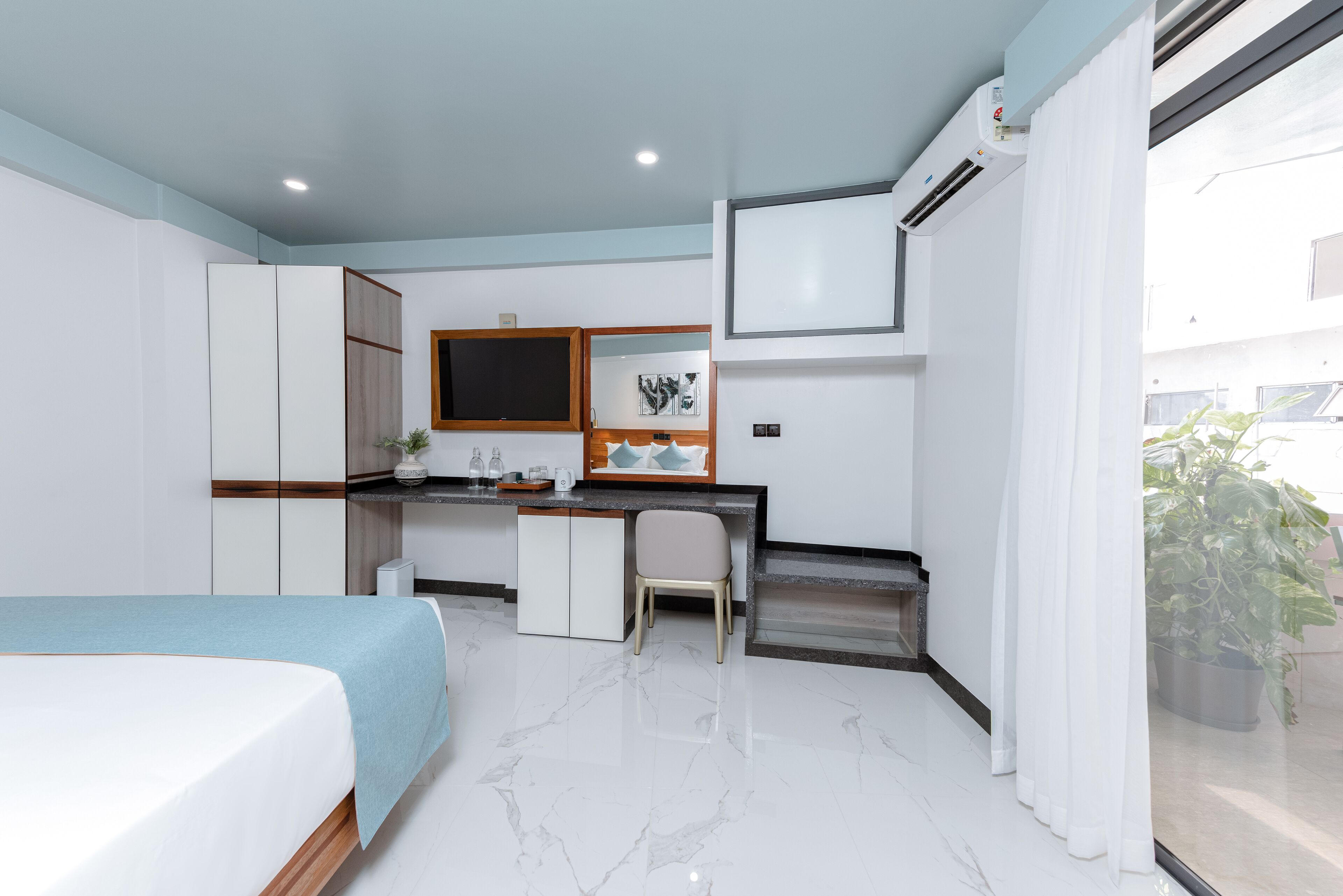 A modern hotel room with a bed, a desk, a chair, and a small kitchenette.