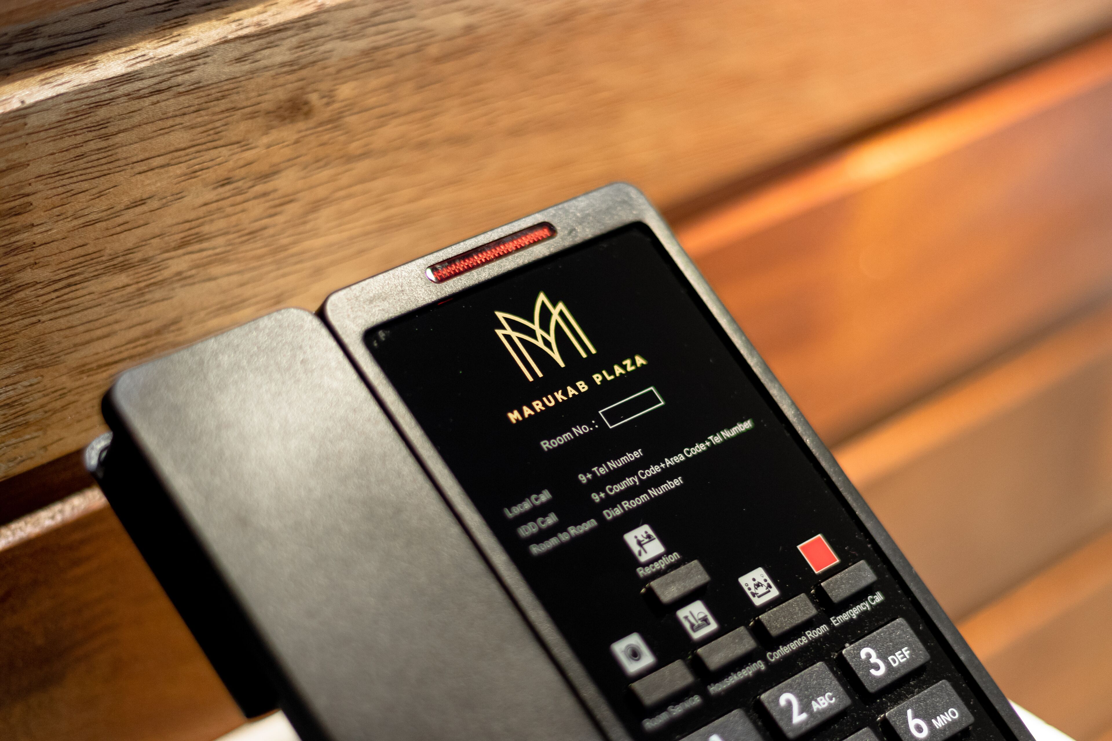 Bedieningspaneel in een hotelkamer, met een keypad en een scherm waarop de naam van het hotel staat: Marukab Plaza.