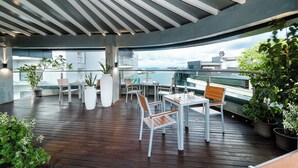 A covered outdoor seating area with tables and chairs, potted plants, and a view of the sea. - Marukab Plaza (Malé)
