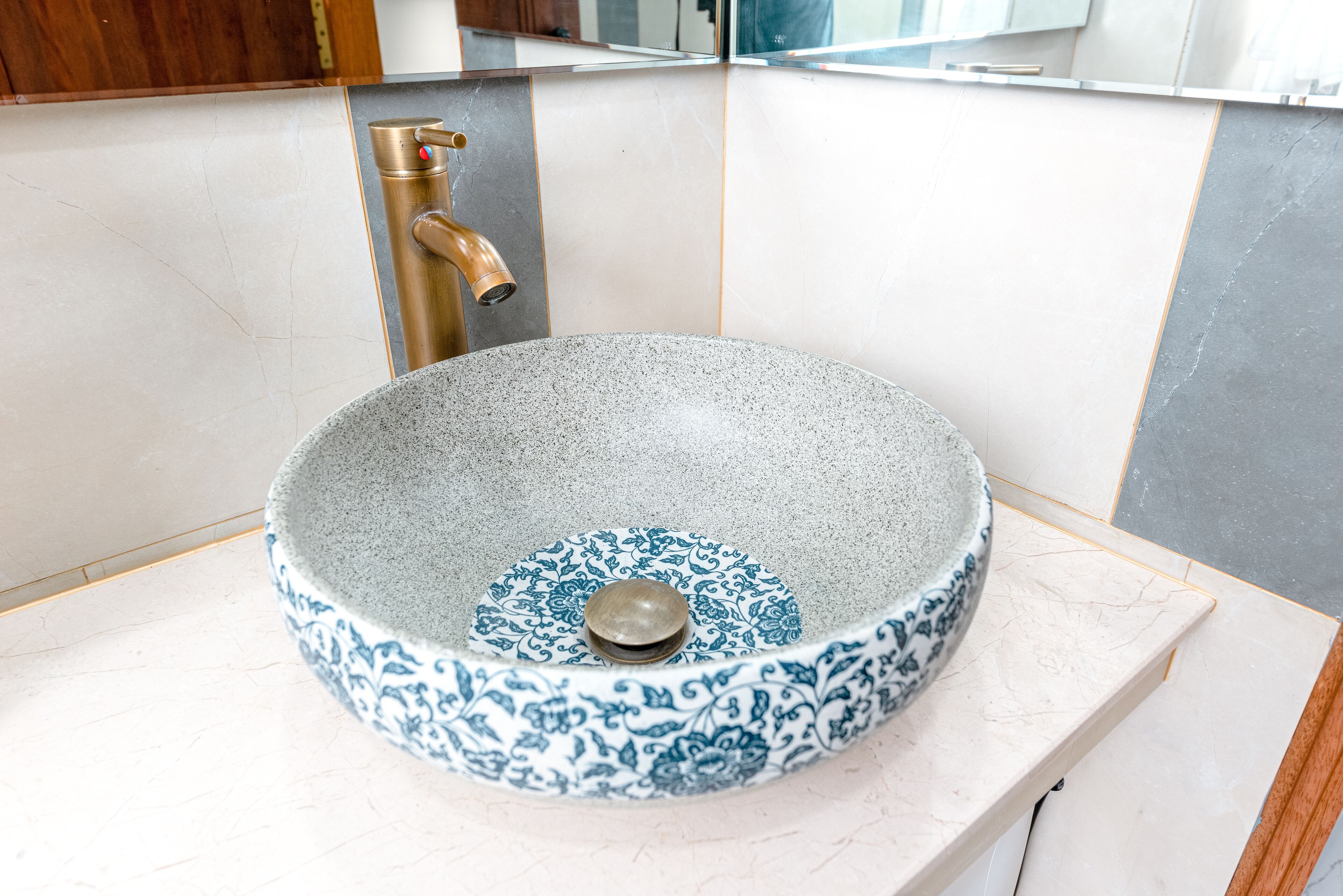 A bathroom with a round, blue and white patterned sink, a gold faucet, and a white countertop.