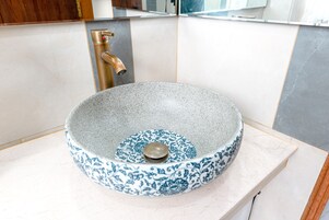 Un baño con un lavabo redondo, de diseño azul y blanco, un grifo dorado y una encimera blanca.