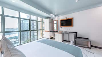 A modern hotel room with a large bed, a desk, a television, and a view of the city through large windows.