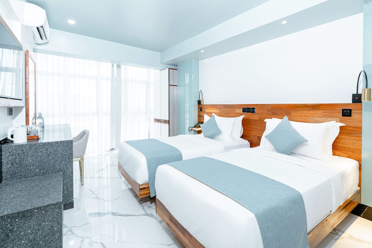 Une chambre d’hôtel moderne avec deux lits, un bureau et une grande fenêtre.