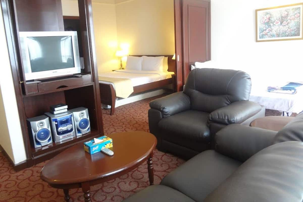 A hotel room with a bed, a television, a sofa, a coffee table, and a desk with speakers.