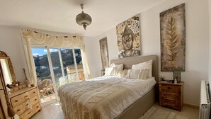 A bedroom with a large bed, a dresser, a nightstand, and a view of the outdoors.