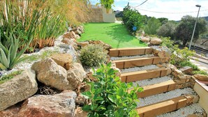 A garden pathway with rocks and plants, leading to a green lawn area.