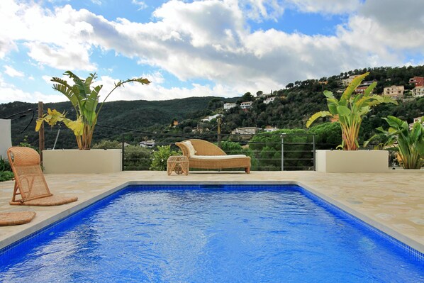 A swimming pool with lounge chairs and potted plants, surrounded by a scenic hillside view.