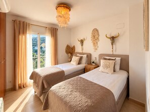 A hotel room with two beds, a chandelier, decorative wall art, and a view through the window. - Holiday house  with private pool in Calonge, Catalonia, Spain for 6 persons (Calonge)