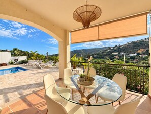 A terrace with a glass table and chairs, a pool, and a view of a hilly landscape. - Holiday house  with private pool in Calonge, Catalonia, Spain for 6 persons (Calonge)