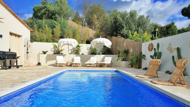 A swimming pool with lounge chairs and umbrellas, surrounded by a landscaped garden and a stone wall.