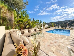 A poolside area with a beige sofa, a glass coffee table, and a clear blue pool. - Holiday house  with private pool in Calonge, Catalonia, Spain for 6 persons (Calonge)