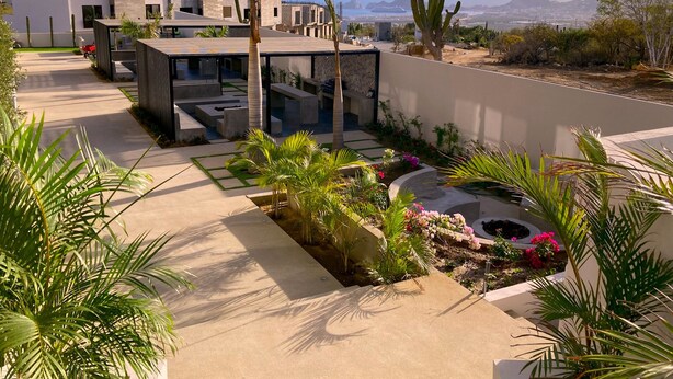 A modern outdoor patio with a pool, surrounded by cacti and palm trees, overlooking a cityscape. - Bahía #304, Sabina Residences (Cabo San Lucas)