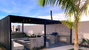 A modern outdoor patio with a pergola, concrete seating, a barbecue grill, and a patterned wall. - Bahía #304, Sabina Residences (Cabo San Lucas)