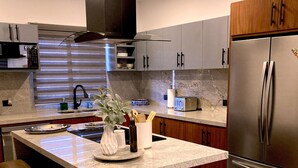 A modern kitchen with a central island, stainless steel appliances, and wooden bar stools. - Bahía #304, Sabina Residences (Cabo San Lucas)