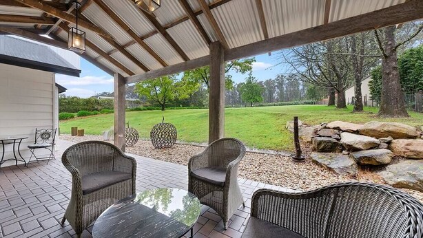A covered patio area with wicker furniture, a table, and a view of a grassy yard.