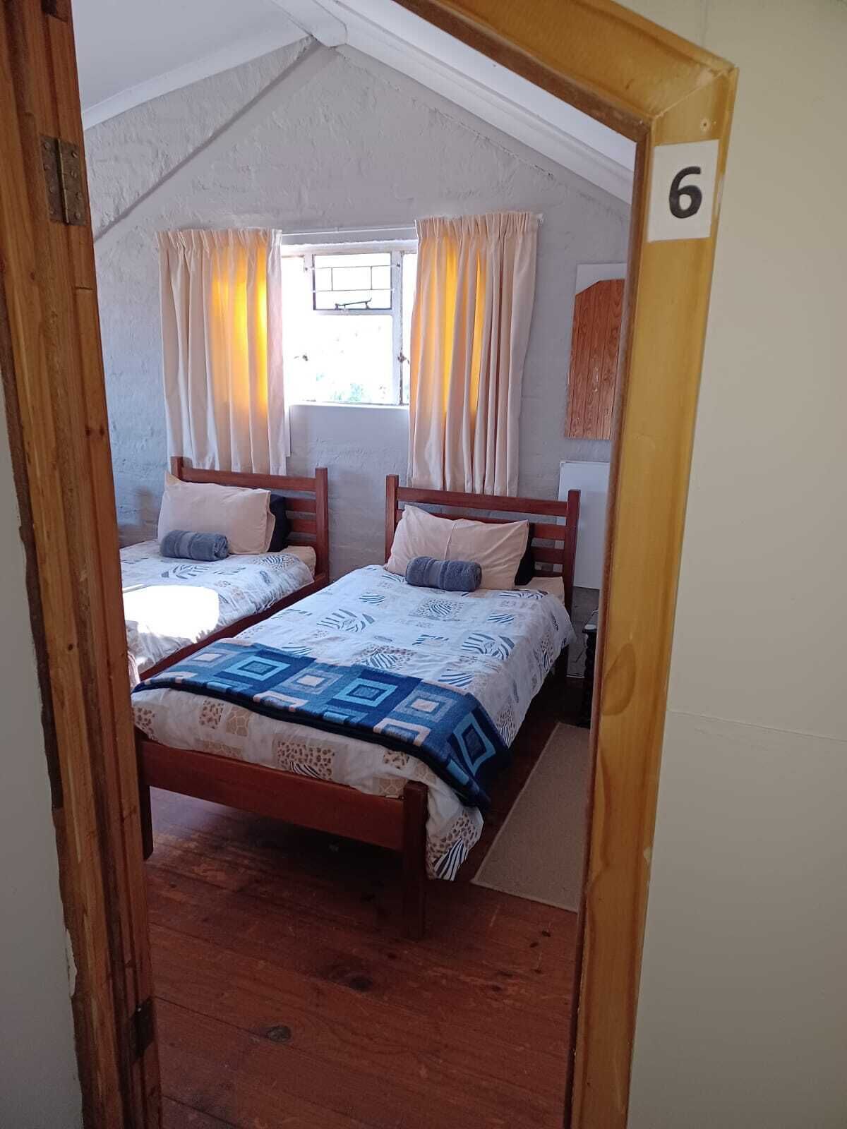 Una habitación con dos camas de madera, cada una con una colcha y almohadas estampadas. Hay una ventana con cortinas, y el techo es inclinado.