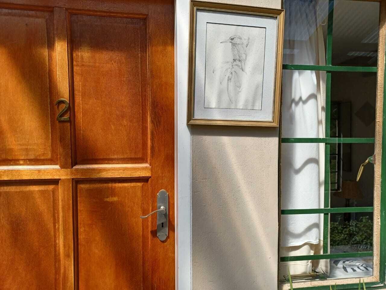 A wooden door with a number '2' and a keyhole, a framed picture on the wall, and a window with green frames and white curtains.