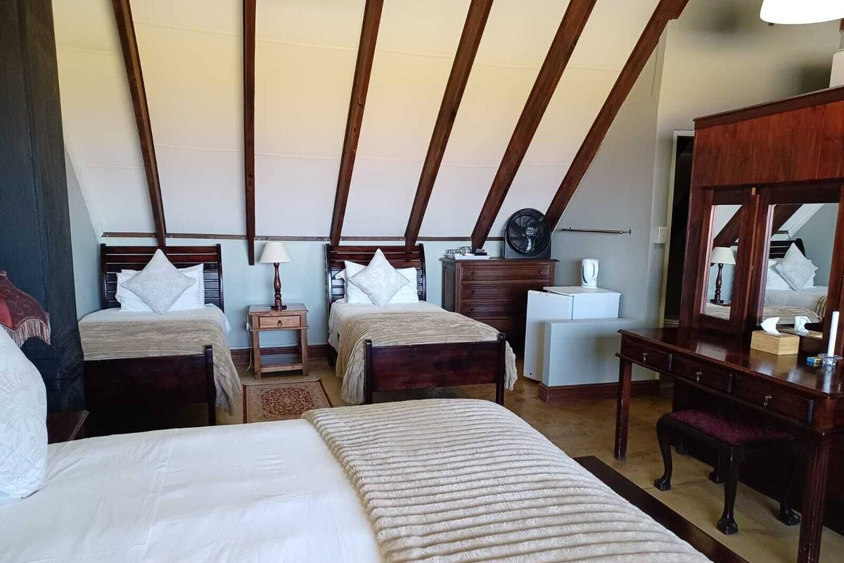 A room with two beds, a desk, a chair, a dresser, a fan, and a mirror.