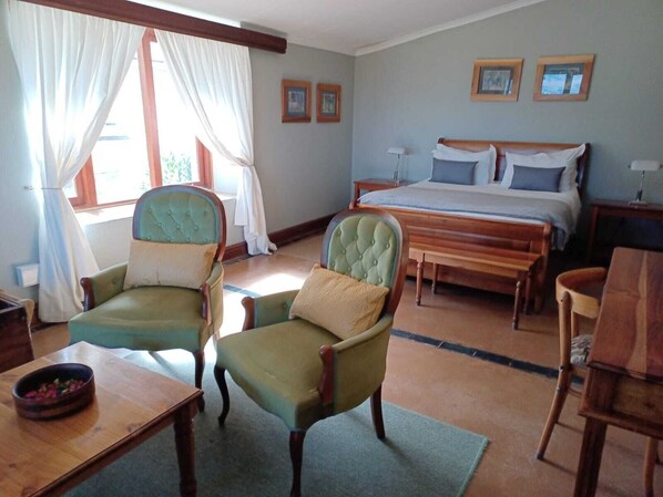 A bedroom with a bed, two armchairs, a wooden table, and a nightstand.