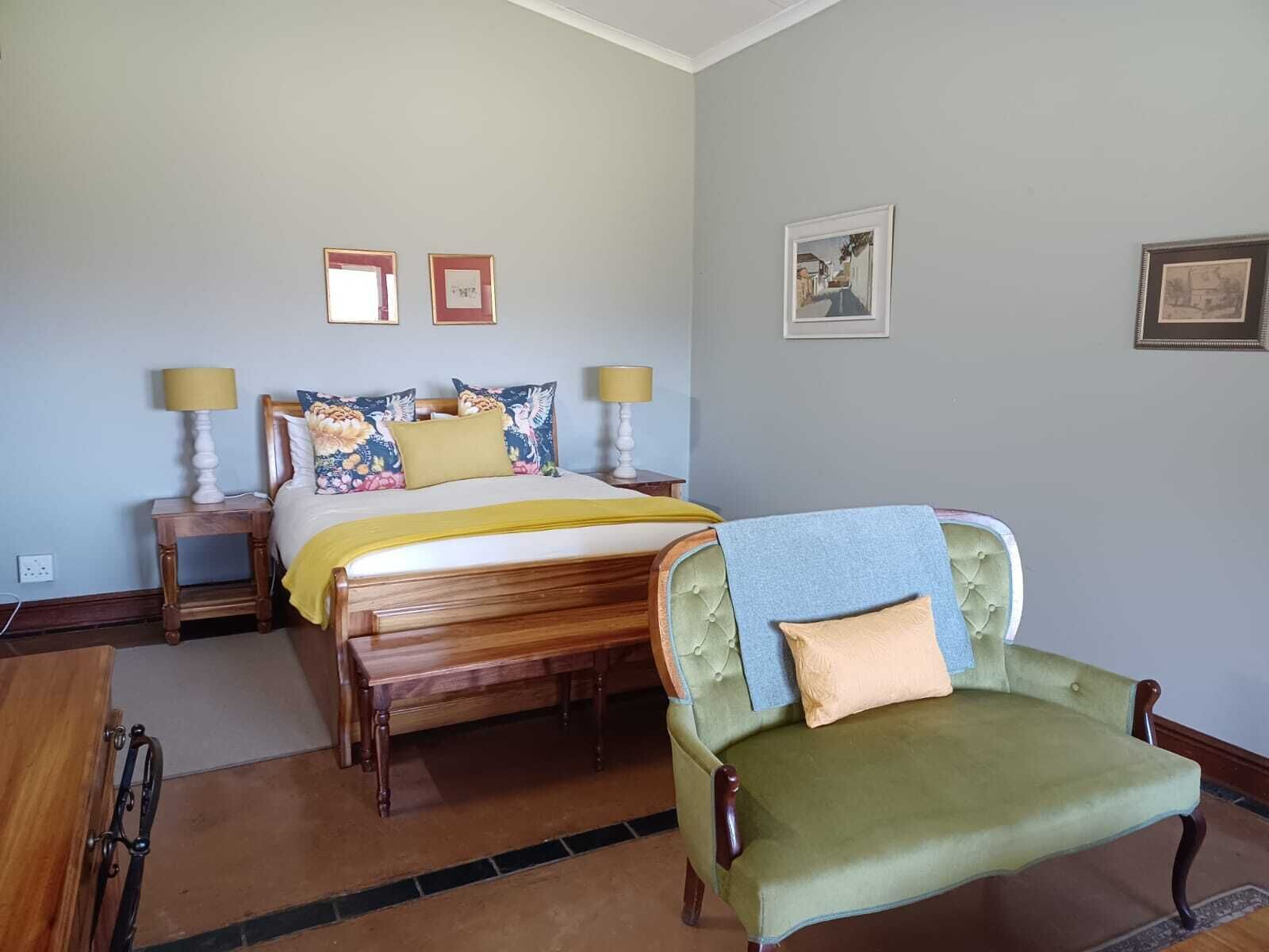 Un dormitorio con una cama, dos mesitas de noche, una silla y cuadros enmarcados en la pared.