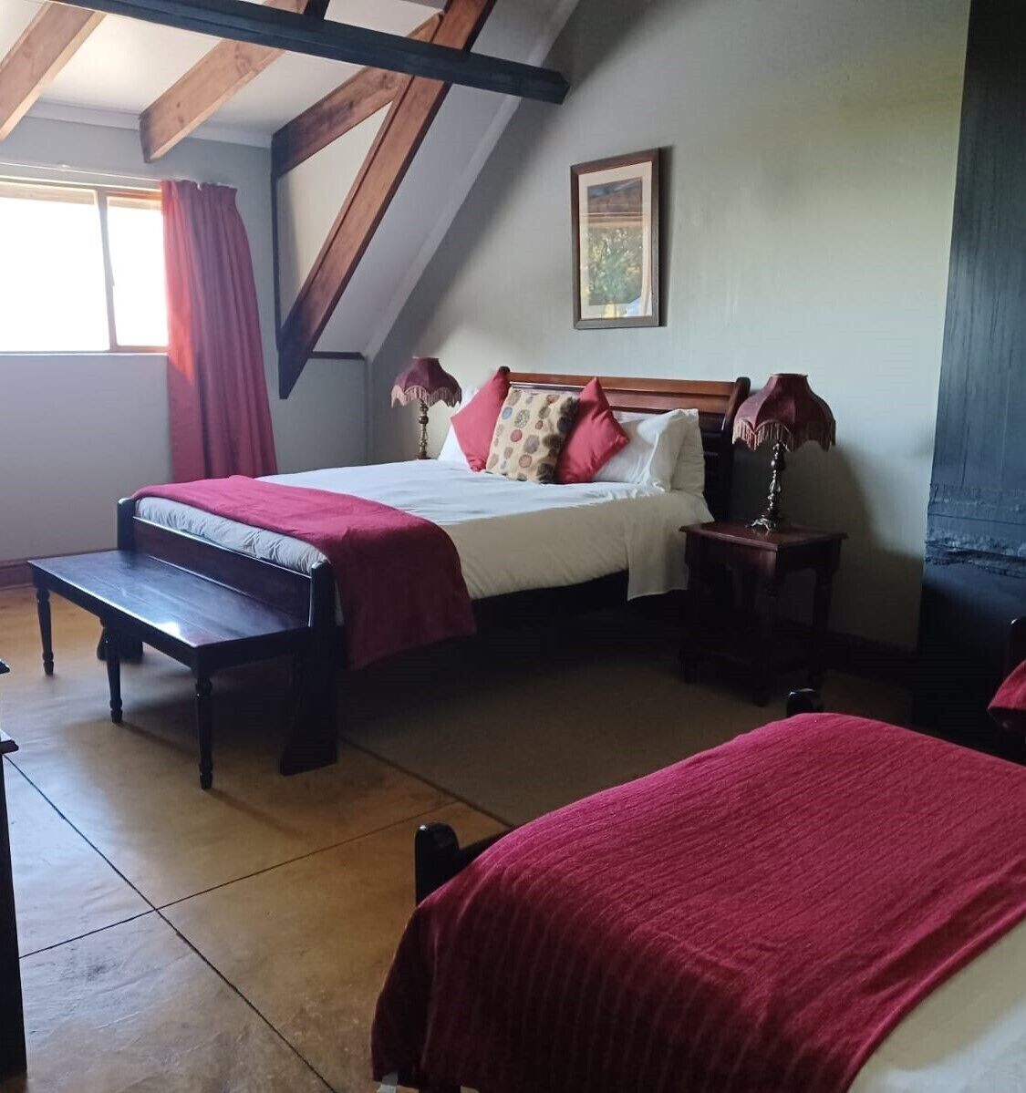 A bedroom with a bed, a bench, a nightstand, and a window with curtains.