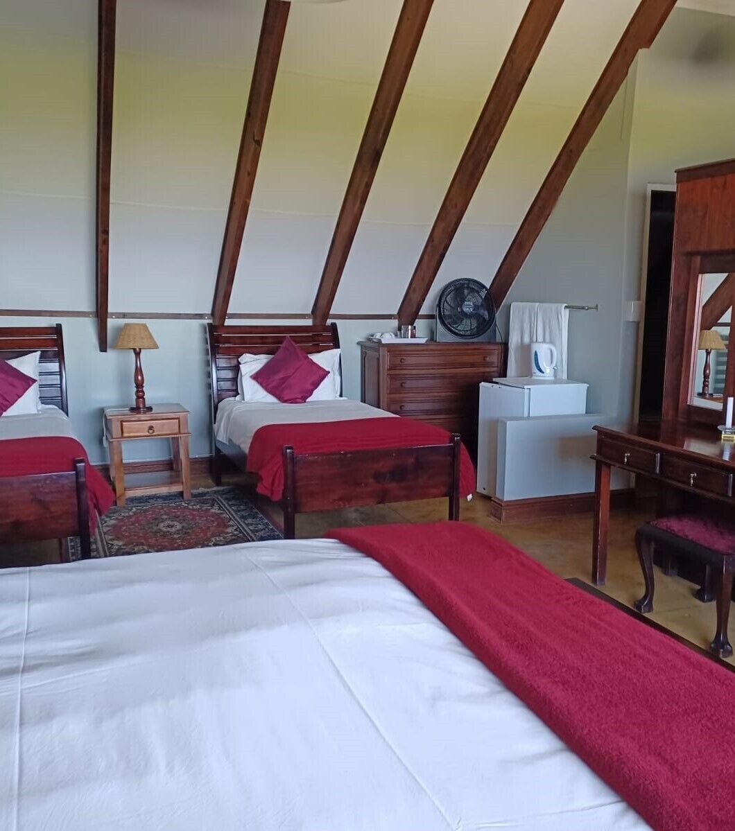 A room with two beds, a wooden dresser, a small desk, a fan, and a mirror.