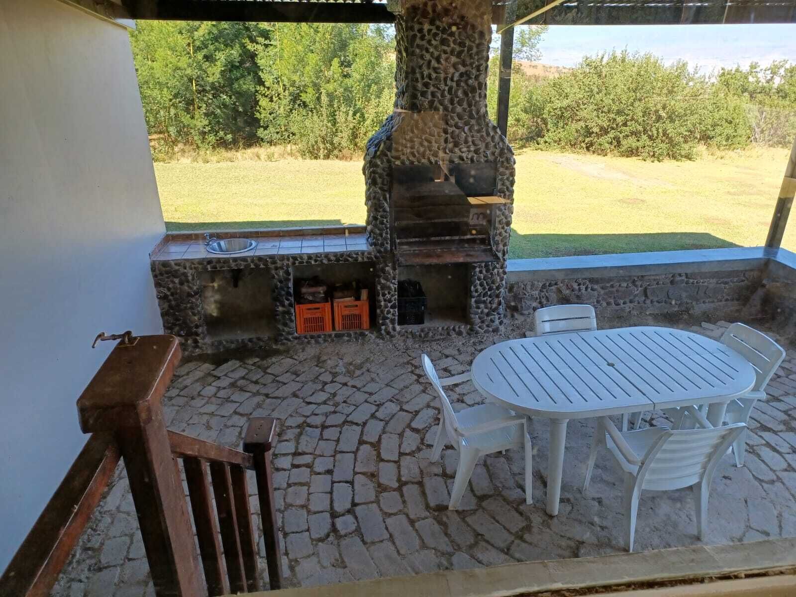 An outdoor patio with a stone barbecue grill, a round table with chairs, and a view of a grassy field.