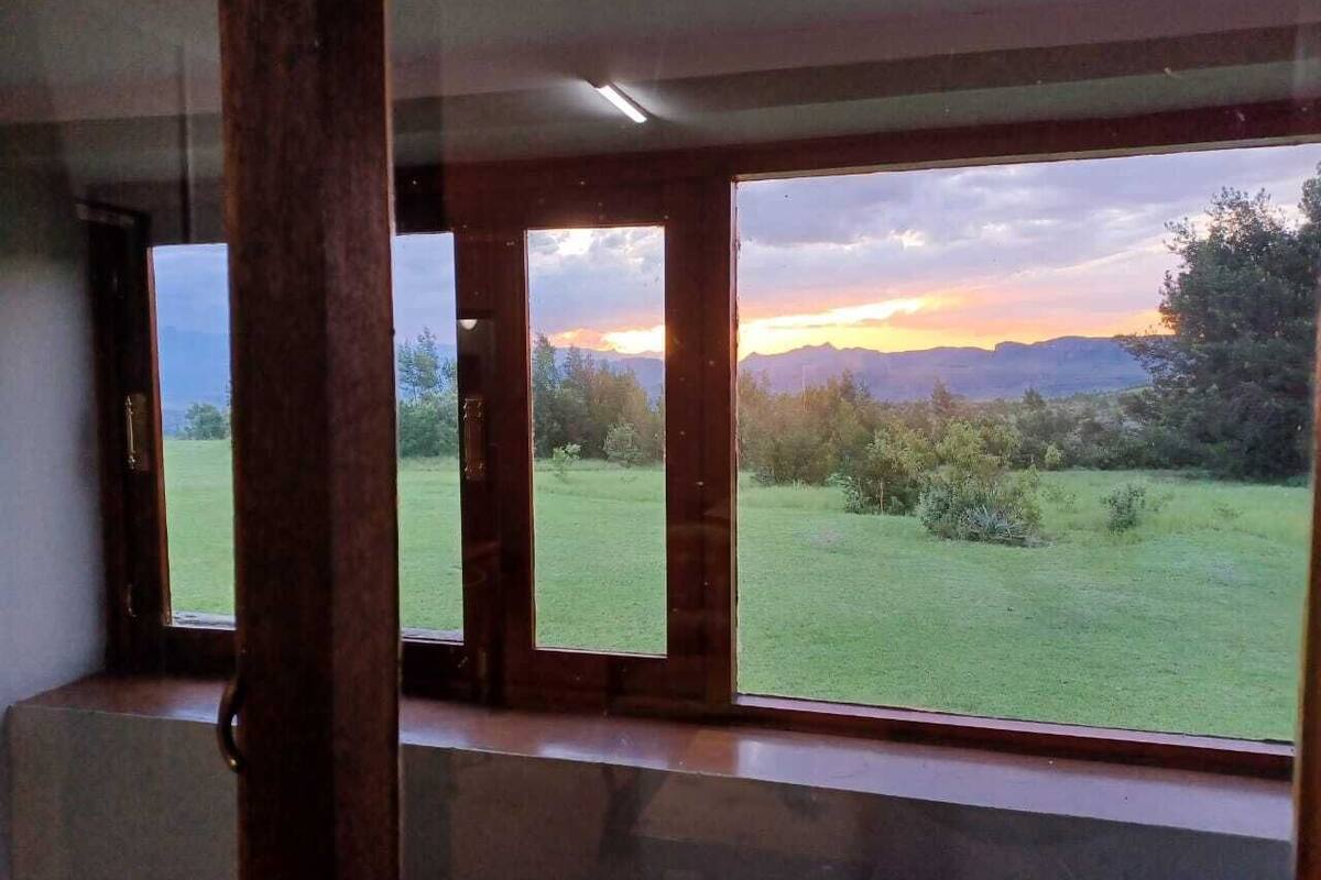 A room with large windows offering a view of a grassy field and distant mountains during sunset.