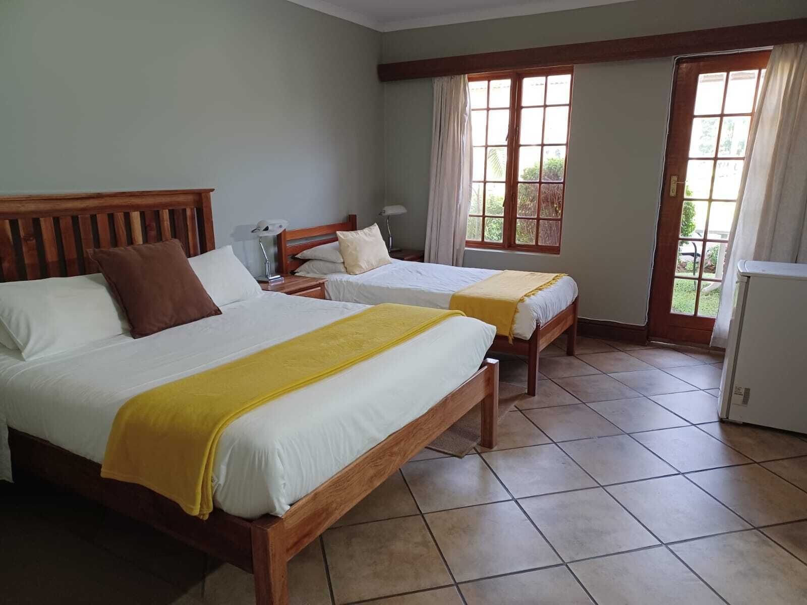 A hotel room with two beds, a wooden headboard, a nightstand, a lamp, and a window with curtains.