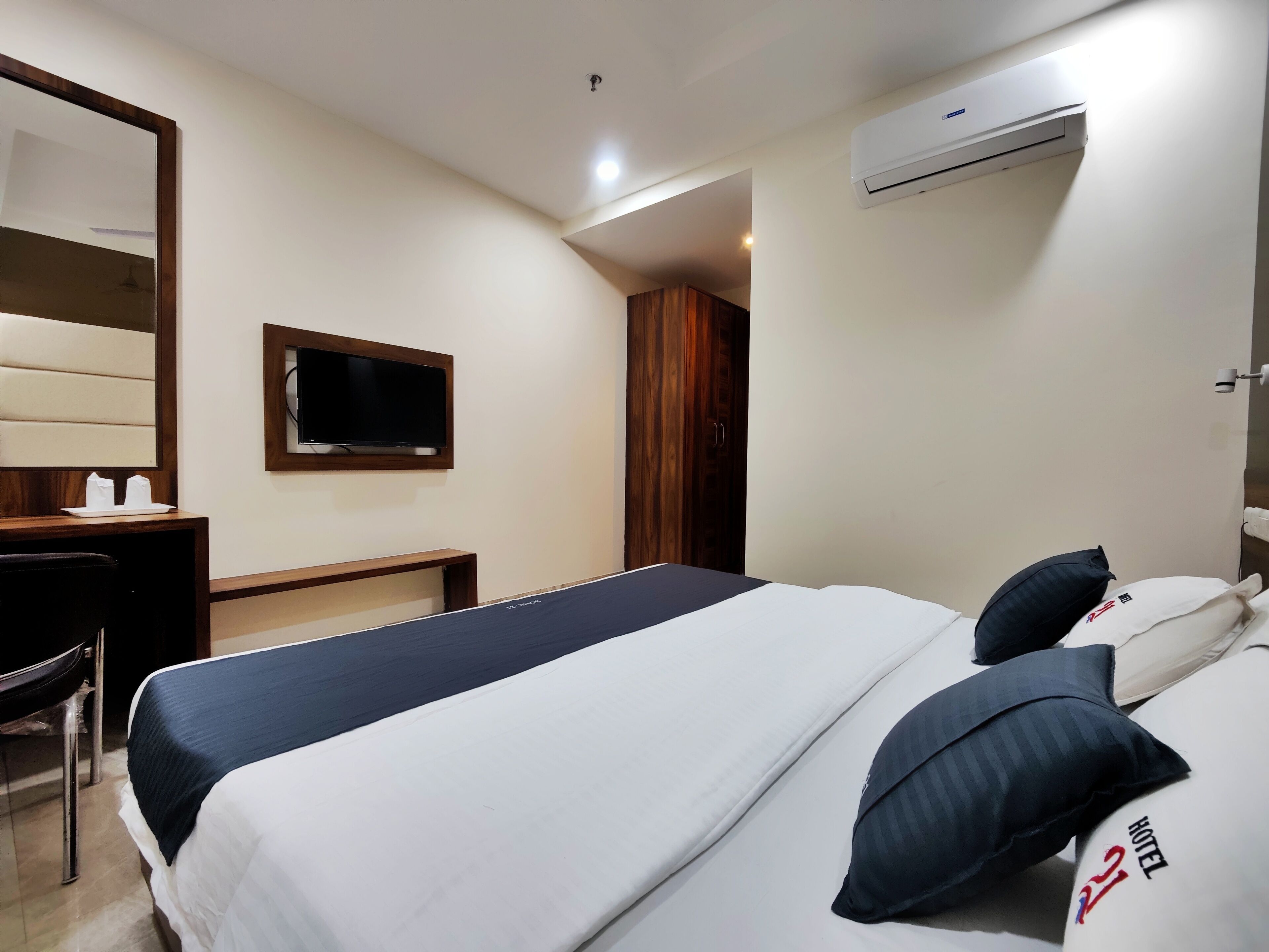 A hotel room with a bed, a desk, a chair, a TV, and an air conditioning unit.