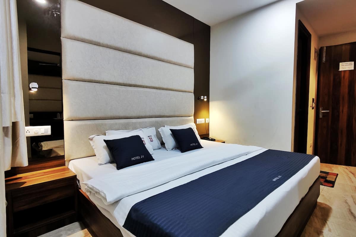 Ein Hotelzimmer mit einem großen Bett, einem Kopfteil mit horizontalen Paneelen, einem Nachttisch aus Holz und einer Tür mit einem Schild.