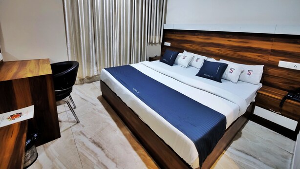 A hotel room with a large bed, a wooden headboard, a desk, and a chair. - Hotel 21 Chandigarh (Chandigarh)