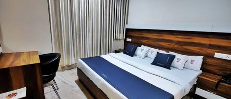 A hotel room with a large bed, a wooden headboard, a desk, and a chair.