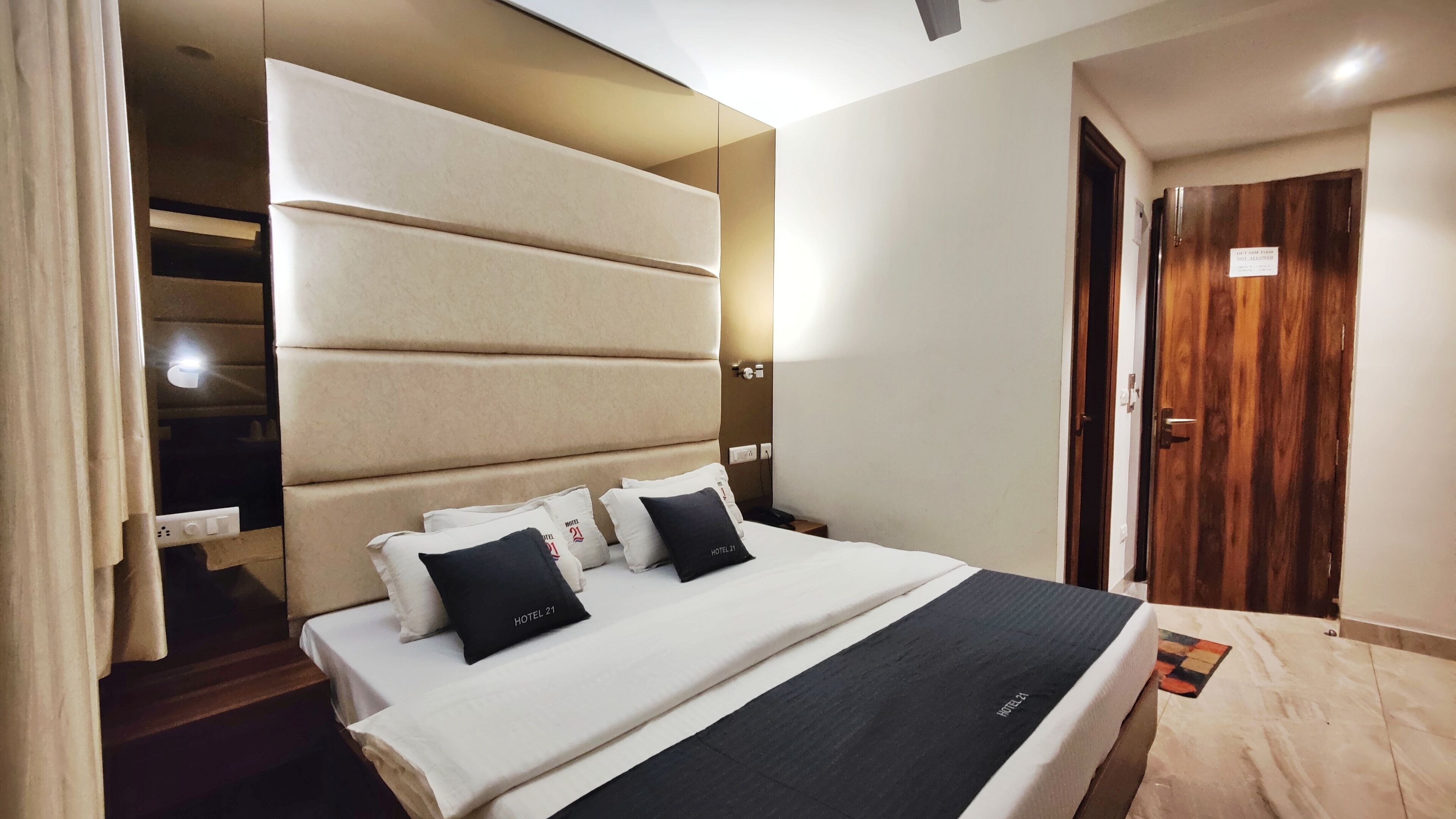 A modern hotel room with a large bed, a headboard with built-in lighting, and a wooden door.