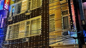 A multi-story building with a sign for "HOTEL 21" and a "HARISH DHARA" sign below. There are two motorcycles parked in front, and the building has multiple windows with string lights. - Hotel 21 Chandigarh (Chandigarh)