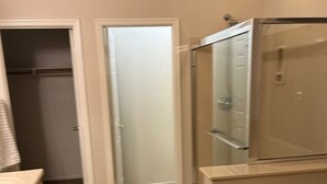 Een badkamer met een inloopdouche, een bad en een toilet. Er is een deur die naar een andere kamer leidt.