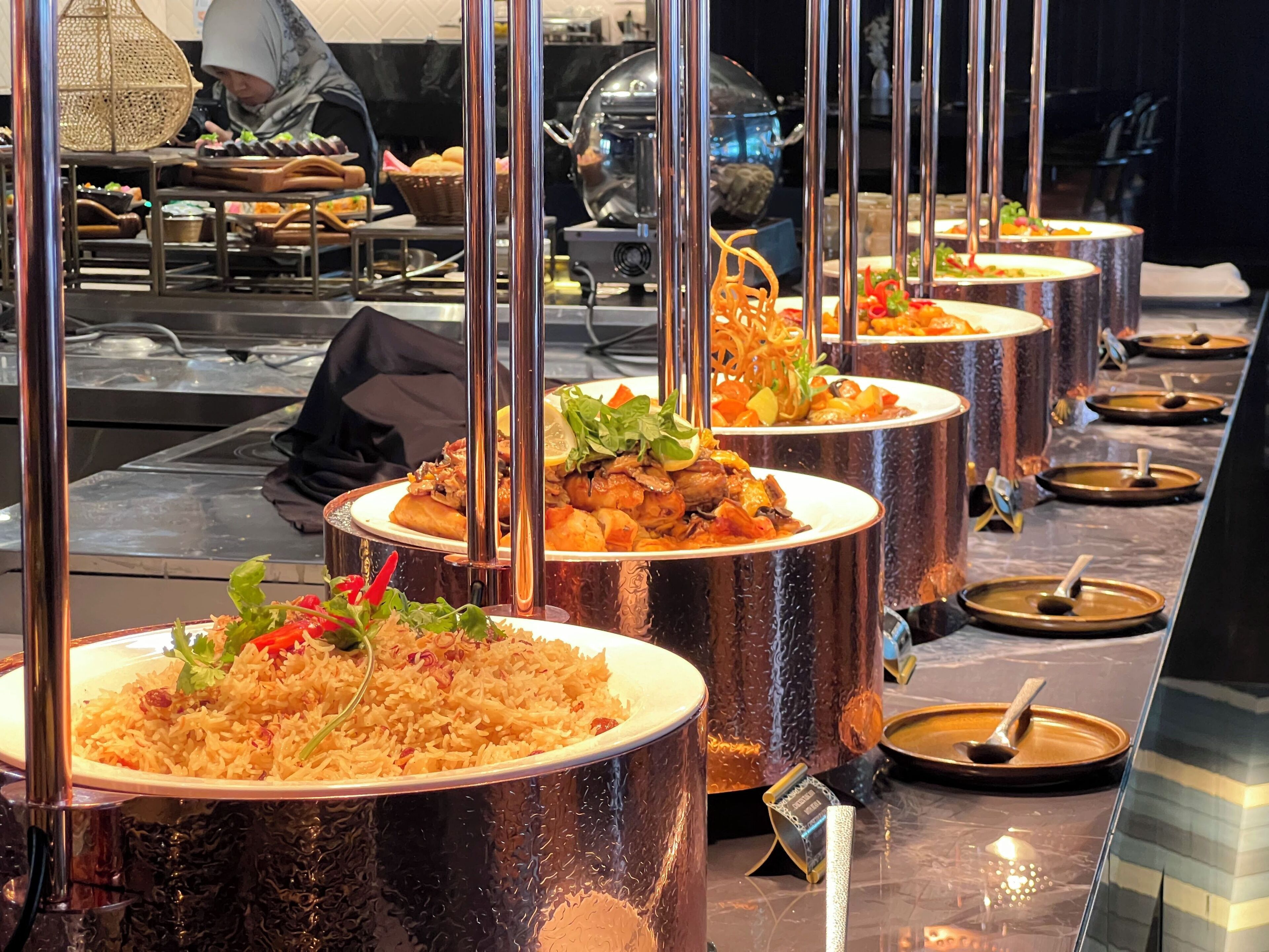 A buffet setup with multiple food stations, each with a large metal bowl containing different dishes.