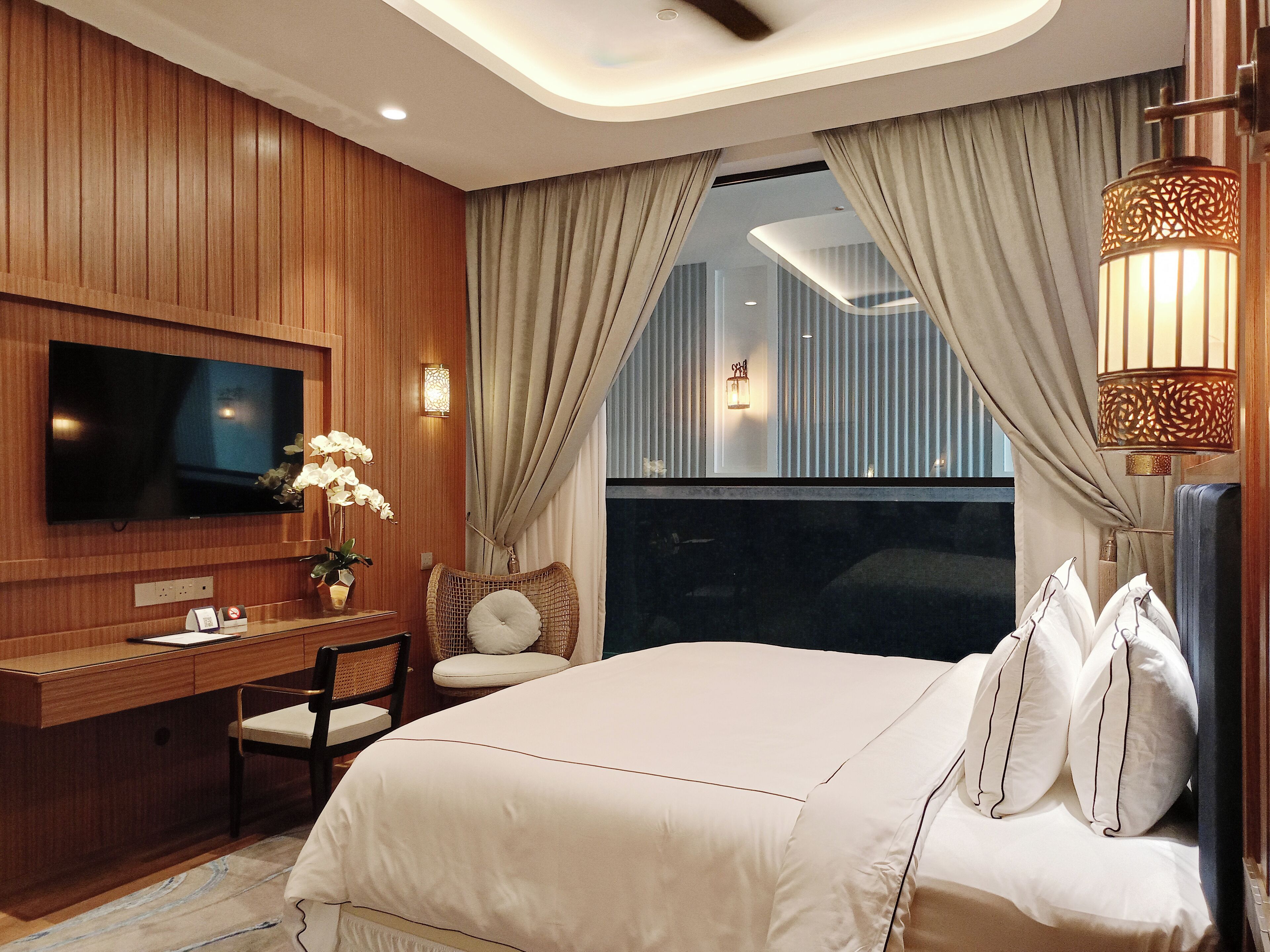 A hotel room with a large bed, a desk with a chair, a television, and a window with curtains.