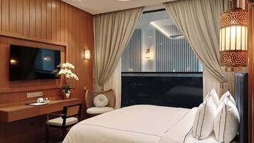 A hotel room with a large bed, a desk with a chair, a television, and a window with curtains.