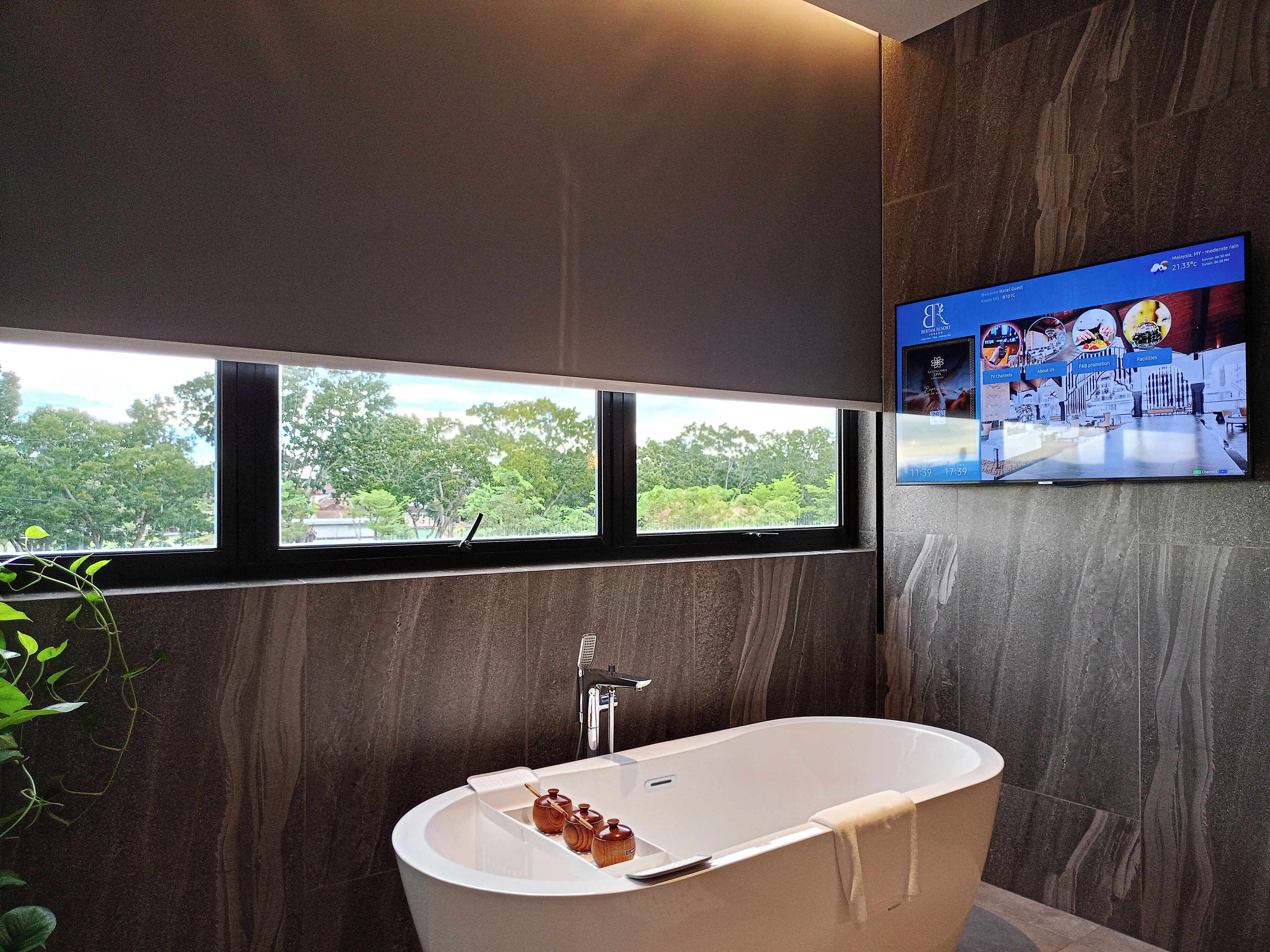 Un bagno moderno con una vasca da bagno indipendente, una finestra con vista sugli alberi e un televisore a schermo piatto montato a parete.