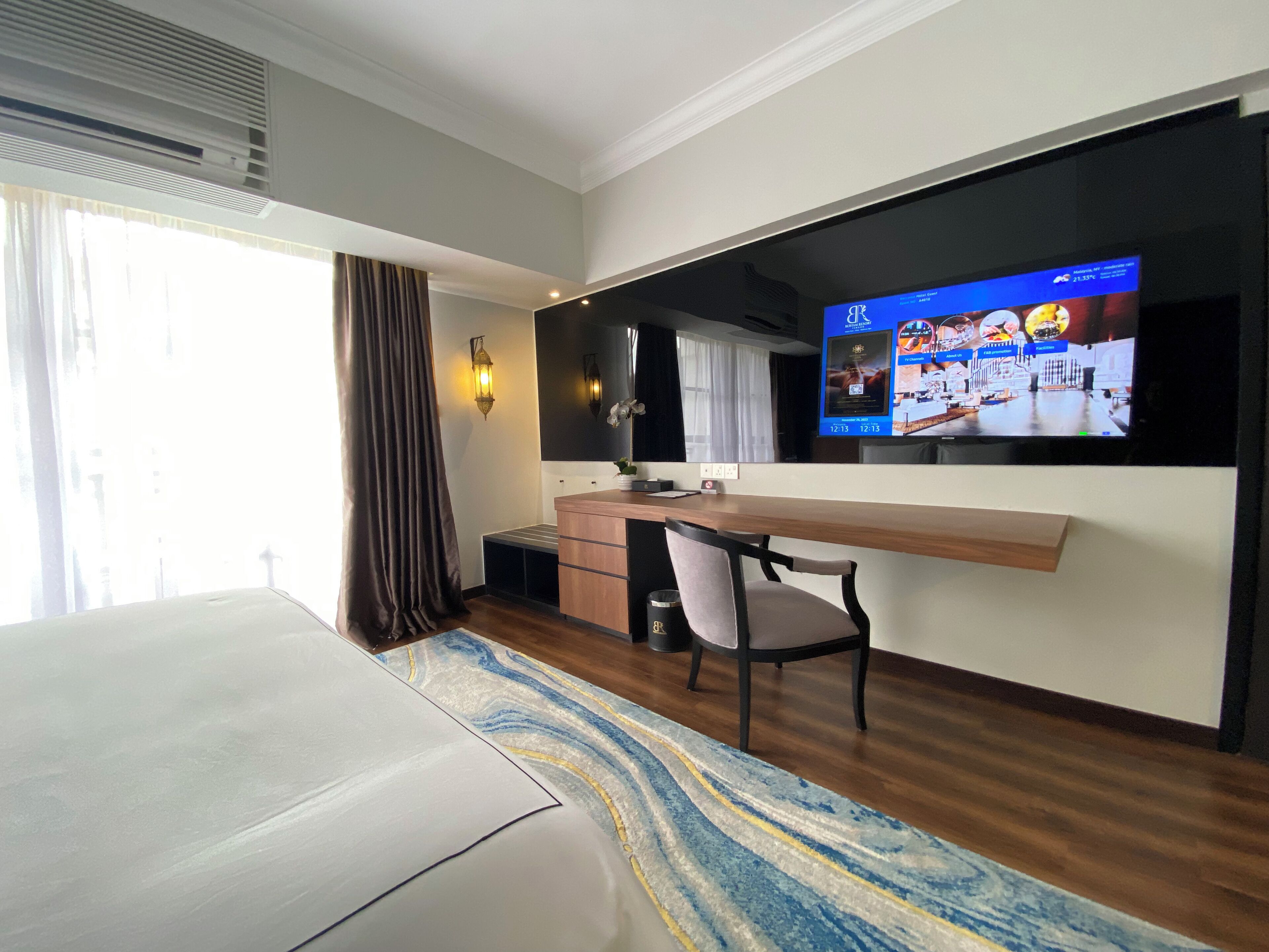 A hotel room with a bed, a desk, a chair, a TV, and a window with curtains.