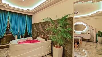 Une salle de bain luxueuse avec une grande baignoire remplie de pétales de roses, un mur en marbre et une plante en pot.